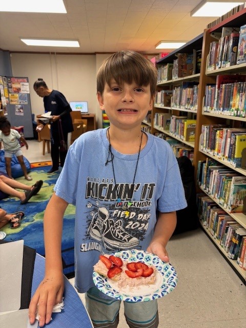 Child in library holding waffle with strawberries, wearing blue 